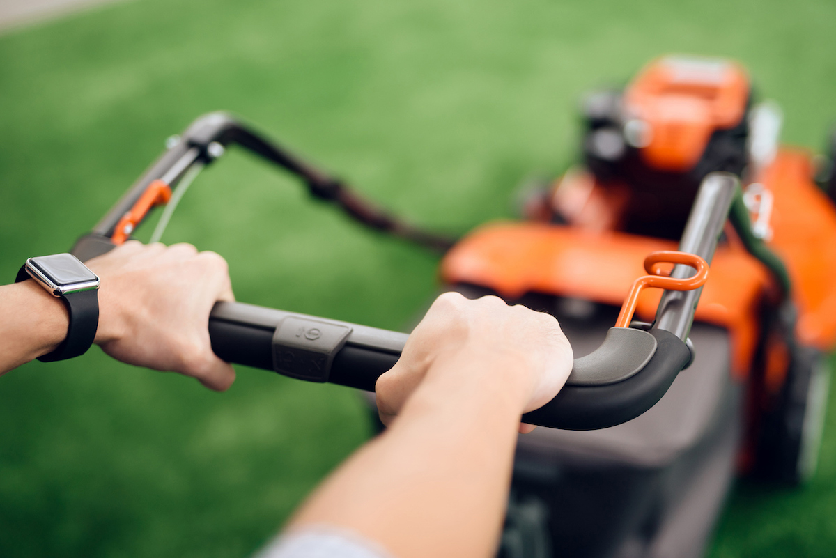 A person is holding an orange and black lawn mower's handle in a pushing position.
