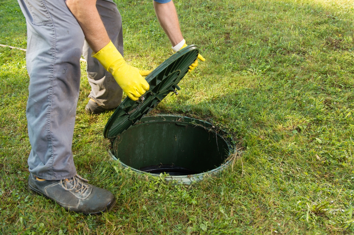 A person is pulling open septic tank lid.
