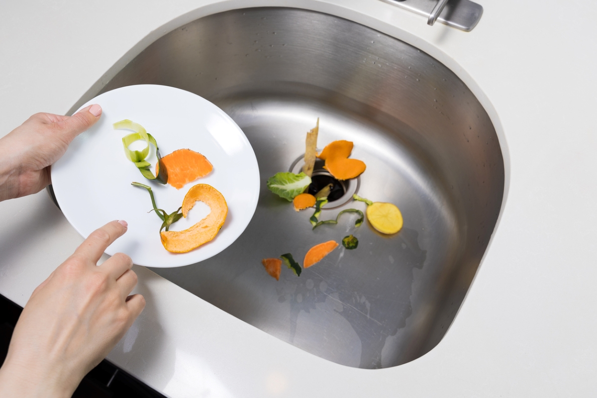Person putting vegetable scraps in sink.