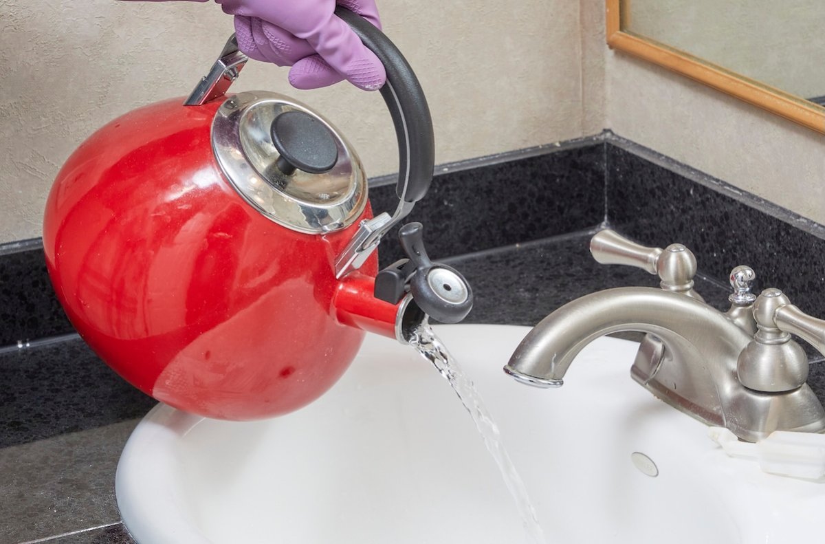 Person pours water from a red tea kettle into a bathroom sink.