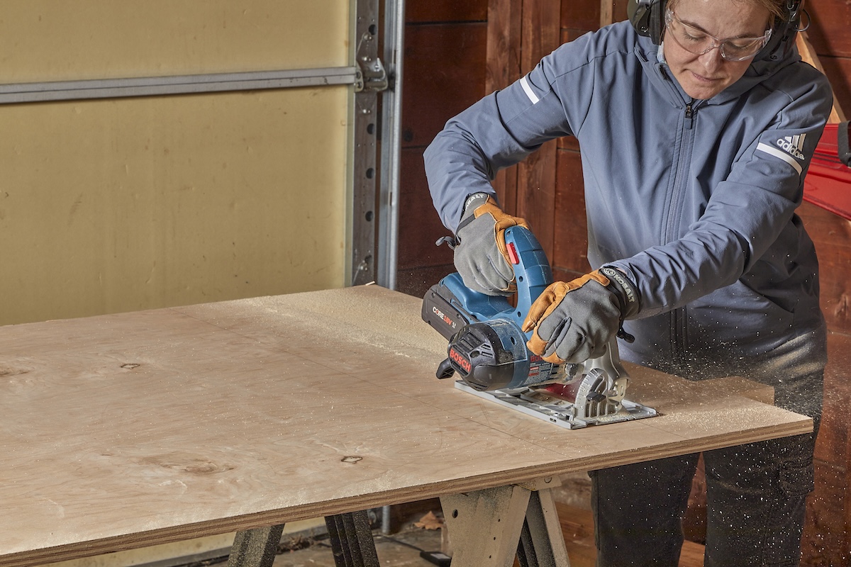 Woman uses a circular saw to make a cross cut on a piece of plywood.