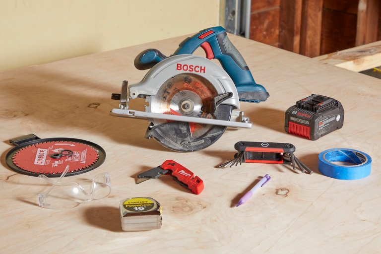 Circular saw on a piece of plywood, surrounded by hex wrench, spare blades, tape, and other supplies.