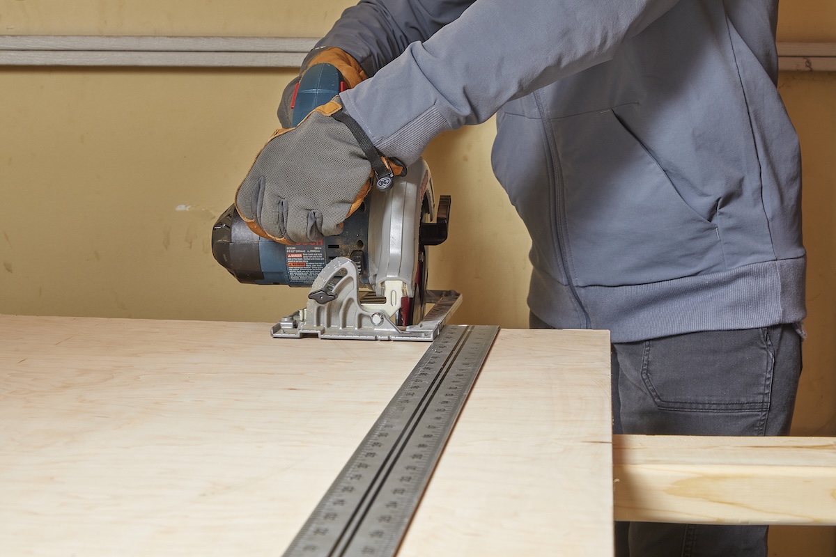 Woman with circular saw uses a metal ruler fence to guide the saw on plywood.