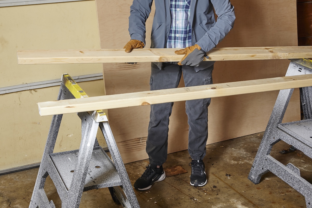 Person sets up 2 2x4s on sawhorses to support heavy plywood.
