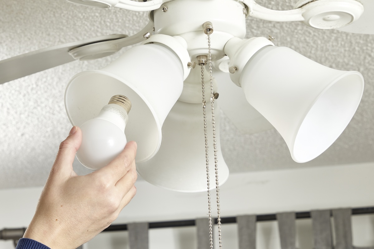 A woman installs a light bulb in a ceiling fan light fixture.