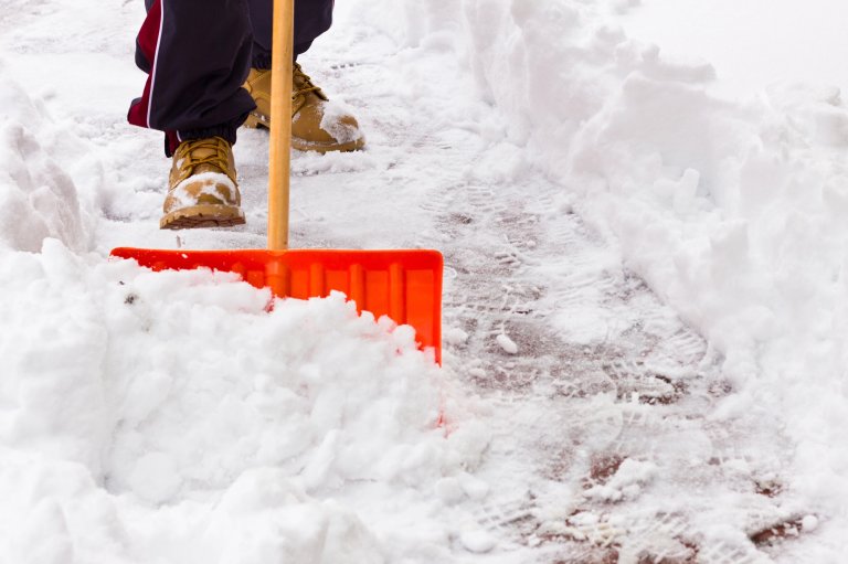 Man pushing a shovel to clear snow from a wintry driveway
