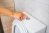 A person is pressing the leftmost button on a dual-flush toilet.