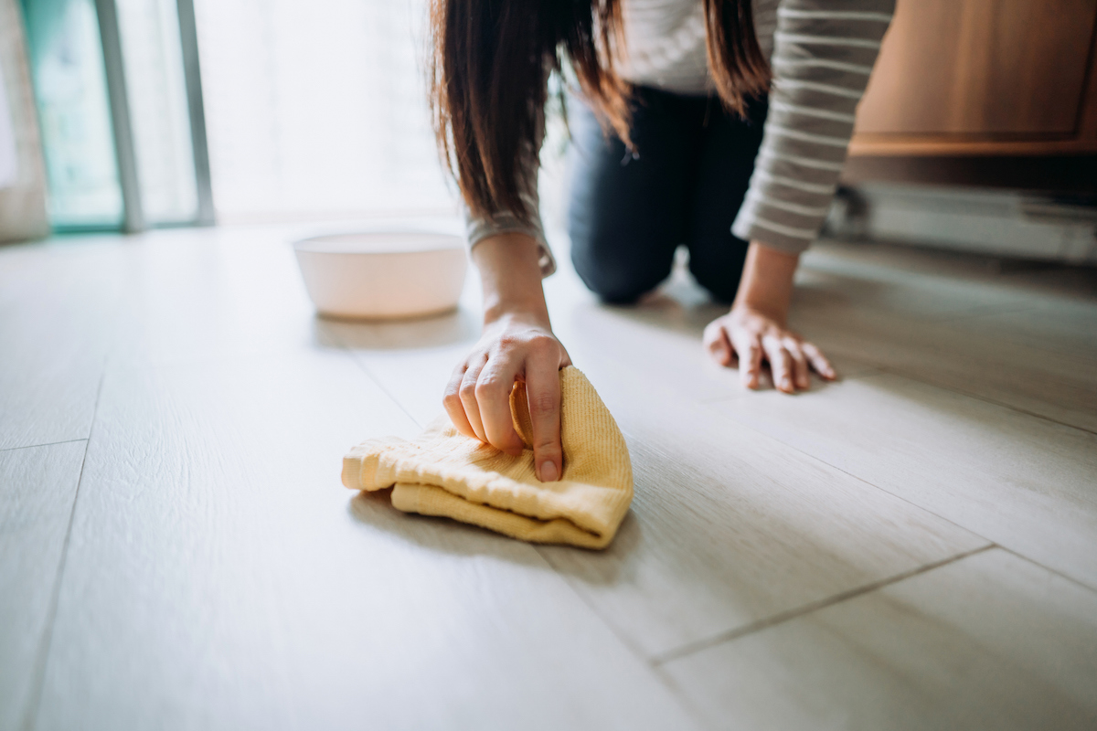 A person is using a rag to clean a spill from a dog bowl on vinyl plank flooring.