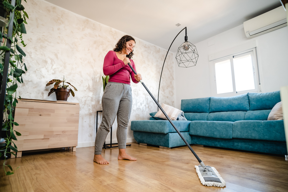 A woman is using a flat dry mop to clean the living room's vinyl plank floor.