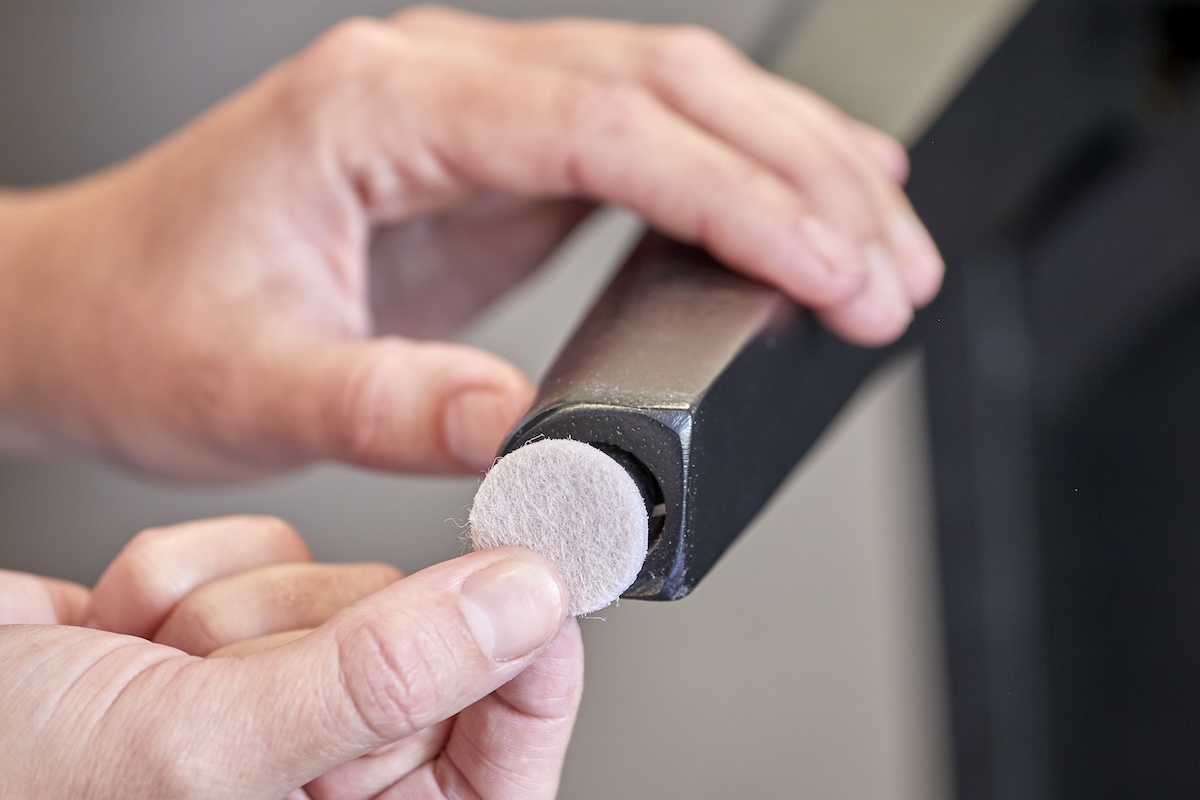 Woman puts a felt furniture pad under a chair leg.