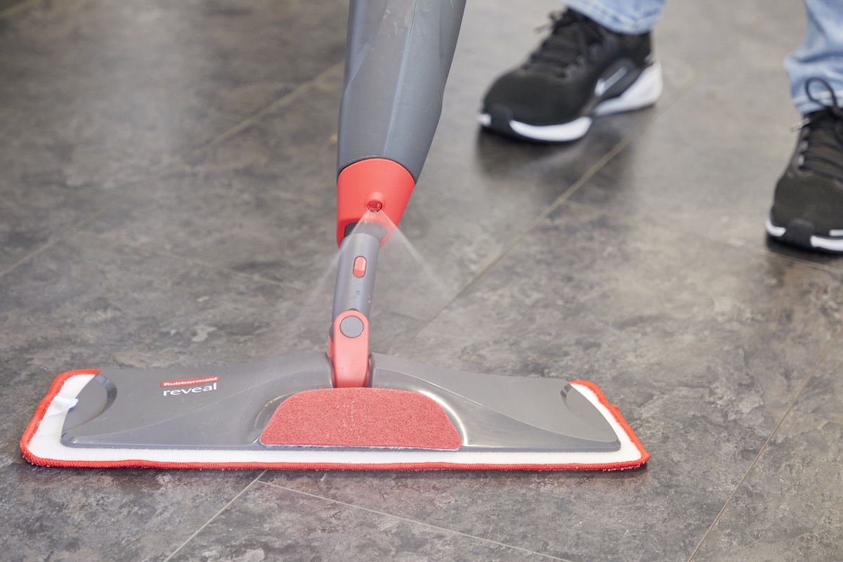 Close up of flat spray mop cleaning vinyl floors, pushed by person wearing jeans and black sneakers.
