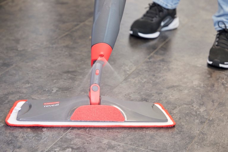 Close up of flat spray mop cleaning vinyl floors, pushed by person wearing jeans and black sneakers.
