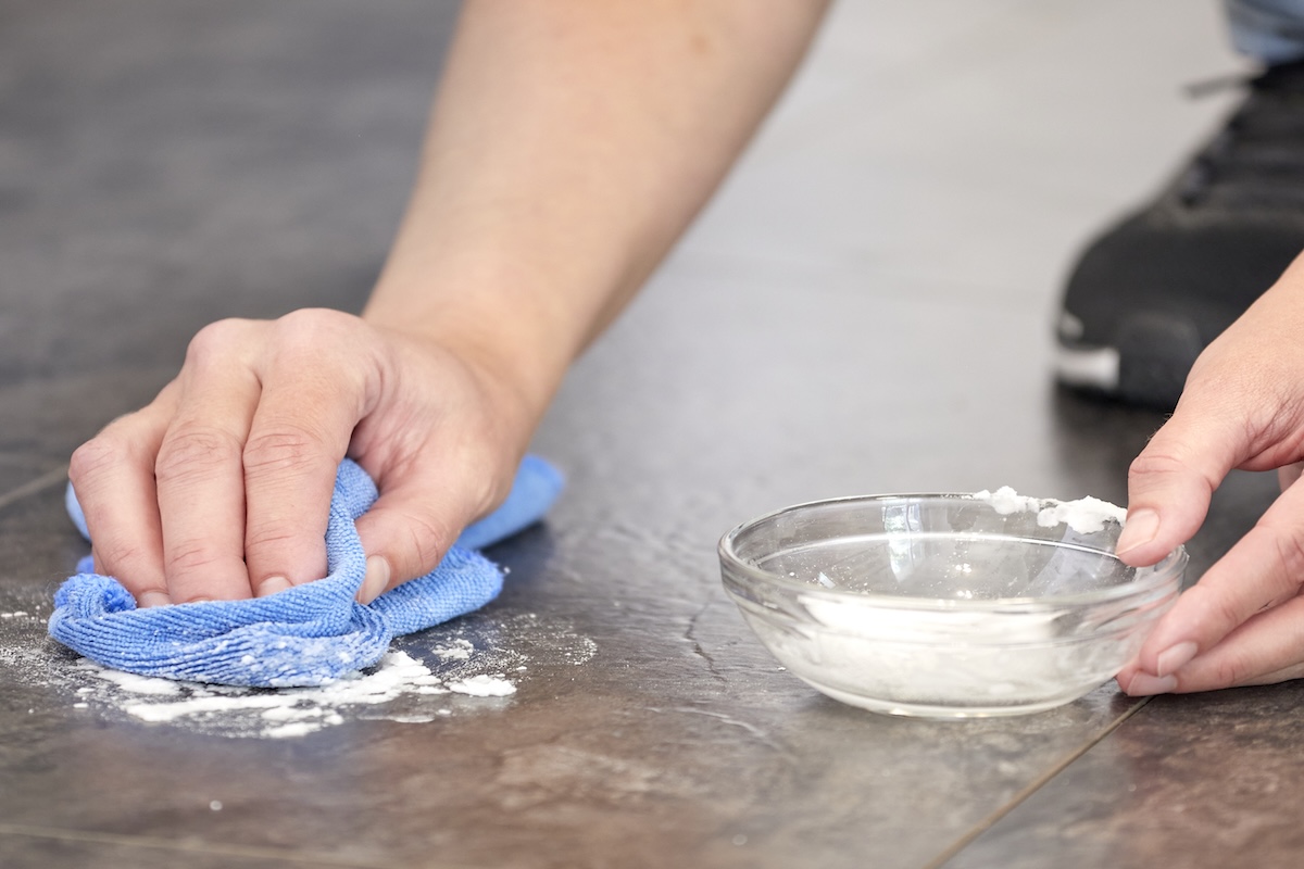 Woman rubs baking soda paste on a vinyl floor with microfiber cloth.