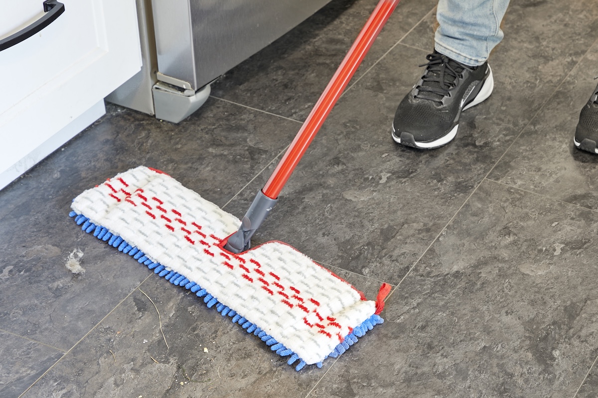 Person wearing jeans and sneakers uses a flat mop to sweep vinyl floors.