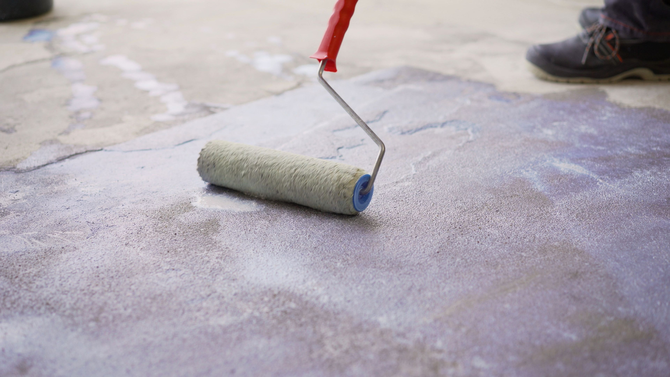 using a white paint roller to prime a concrete floor
