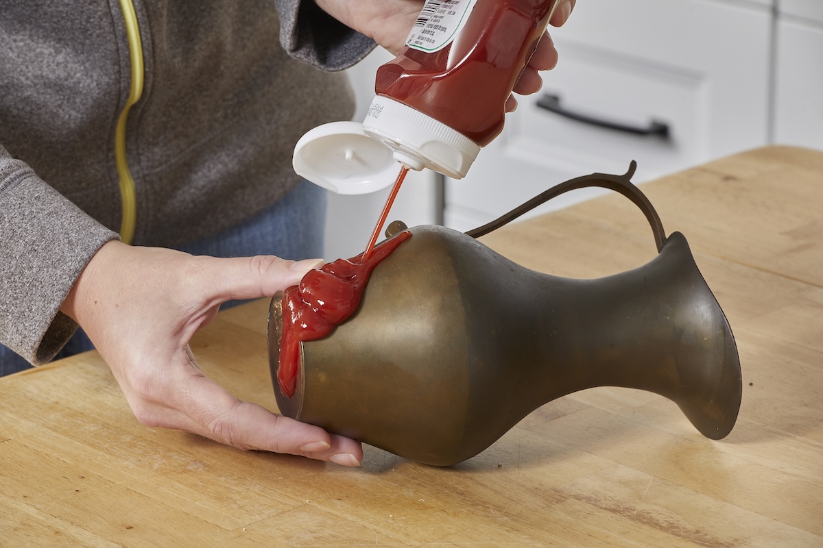 Woman squirts ketchup onto a tarnished brass pitcher.