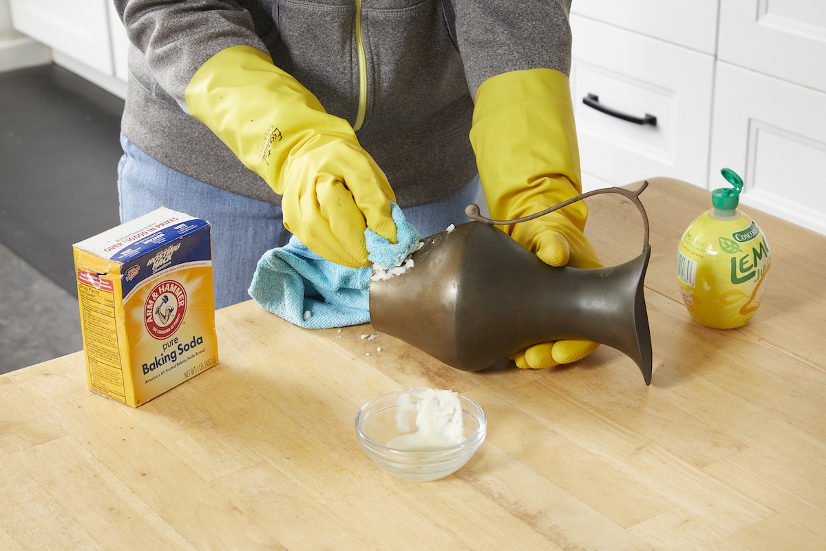 Woman rubs a mixture of lemon juice and salt onto a tarnished brass pitcher.