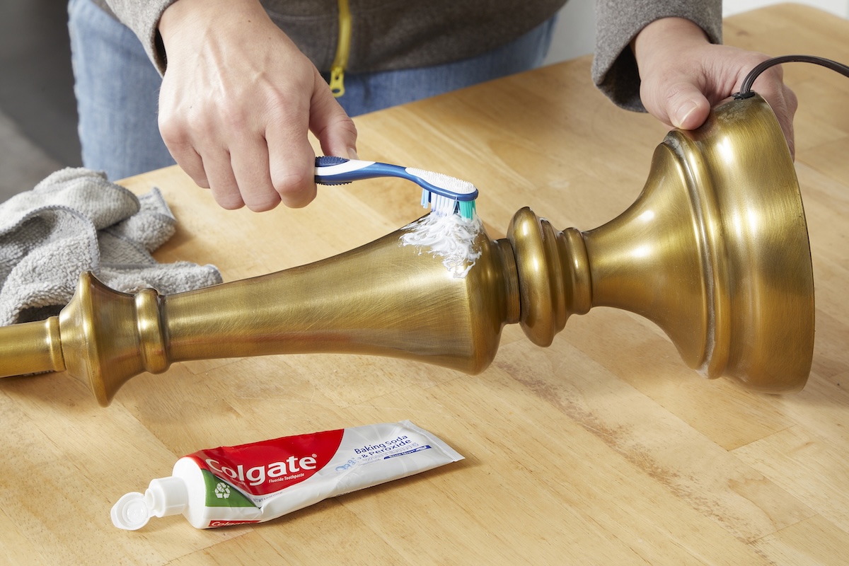 Woman uses toothbrush to apply white toothpaste to a tarnished brass candlestick.