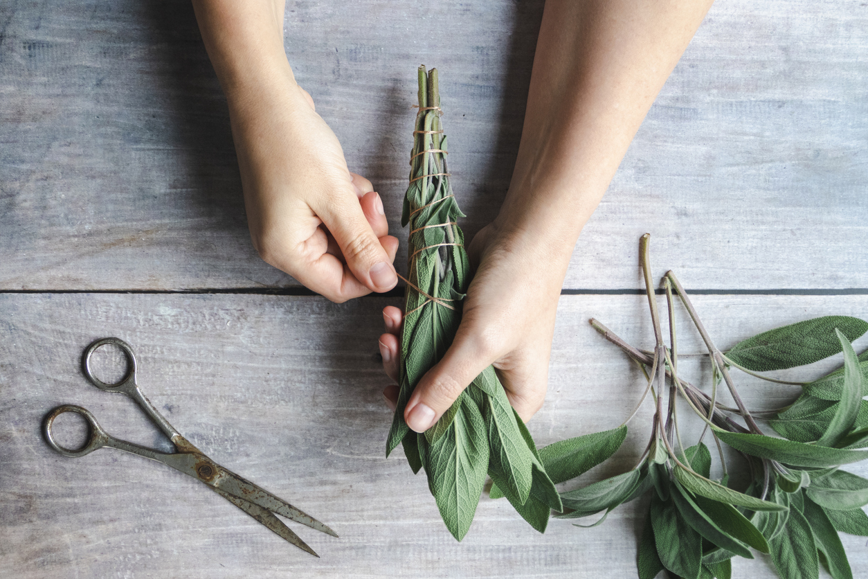 Sage smudge stick making, hands wrap string around sage leaf bundle, natural incense for home and meditation