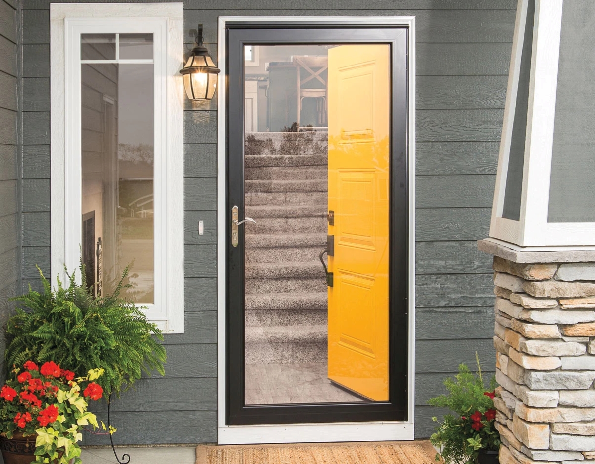 A view of the front entrance clear storm door with an opened yellow door behind it.
