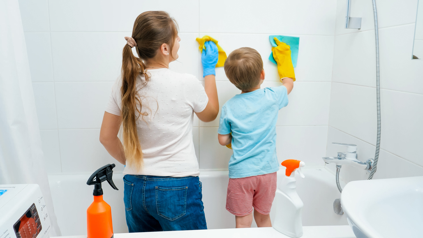 Little toddler boy with young mother washing and cleaning tile walls in bathroom while doing housework and home cleanup.