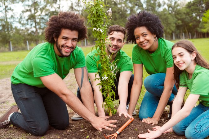 Portrait of smiling volunteers planting together. People in green t-shirts are volunteering for environmental cleanup. They are in park.