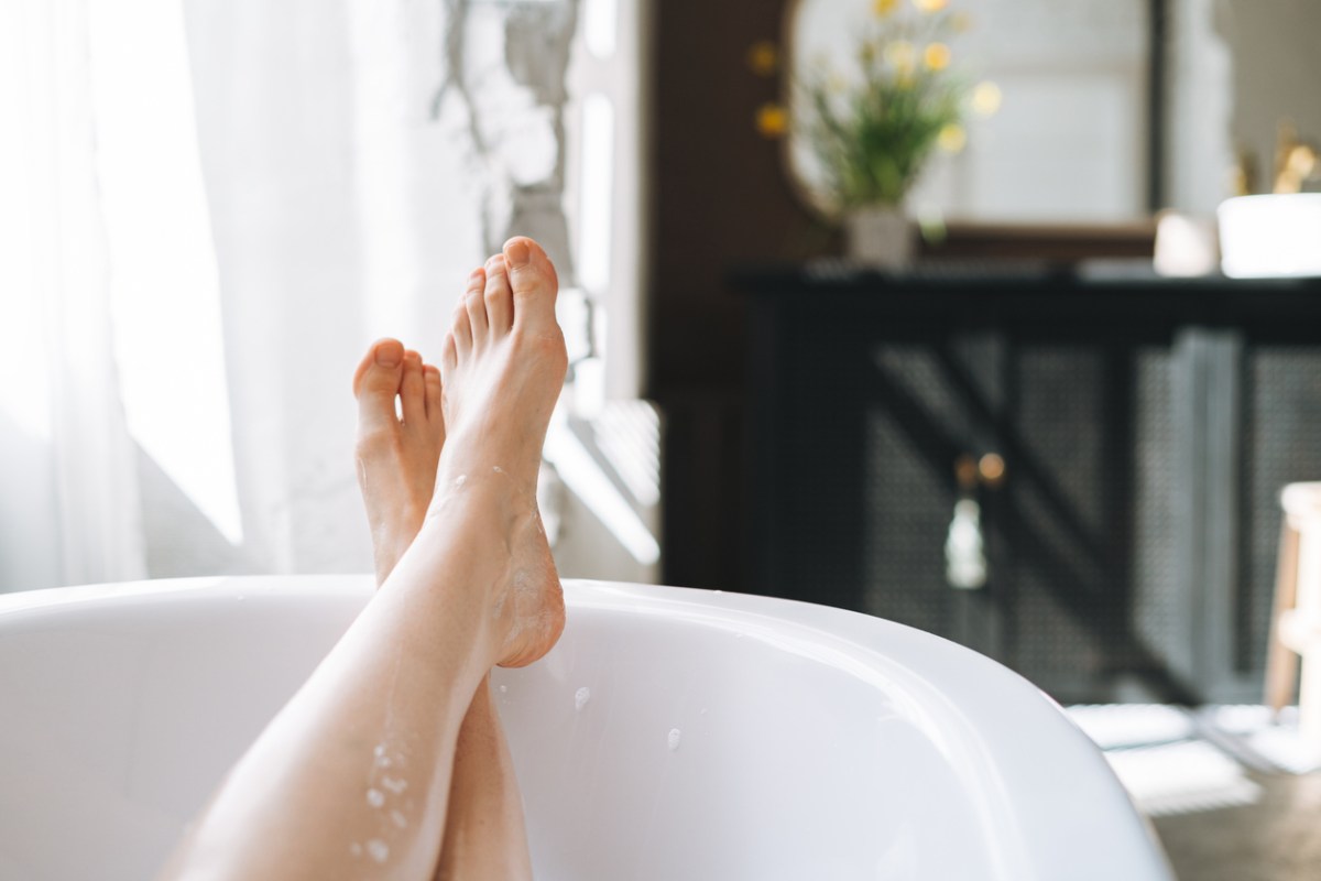 Young women's feet crossed at the edge of a white freestanding bathtub