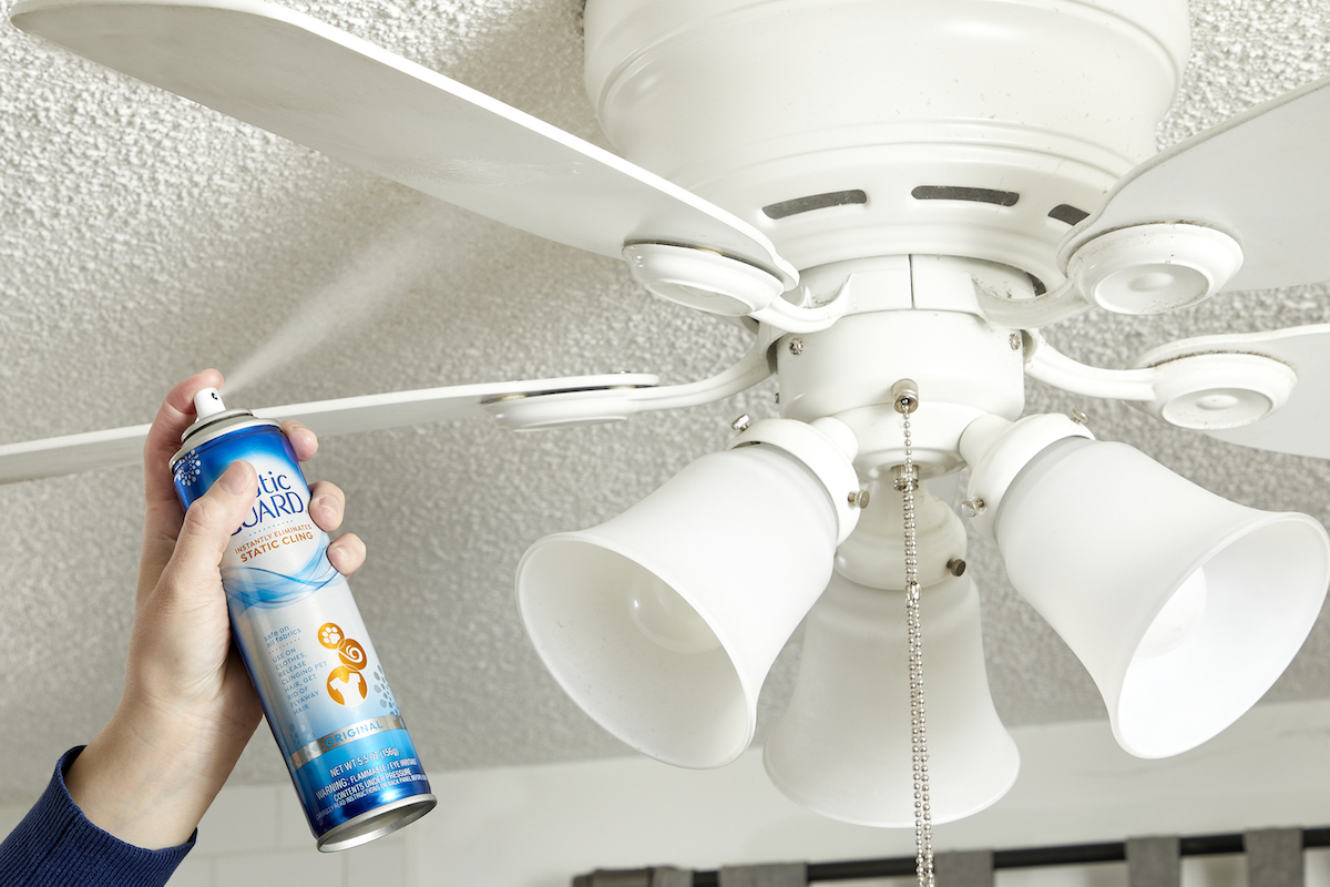 Woman sprays anti-static spray on ceiling fan blades.