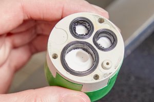 Person holds cartridge from water faucet, inspecting O-rings.
