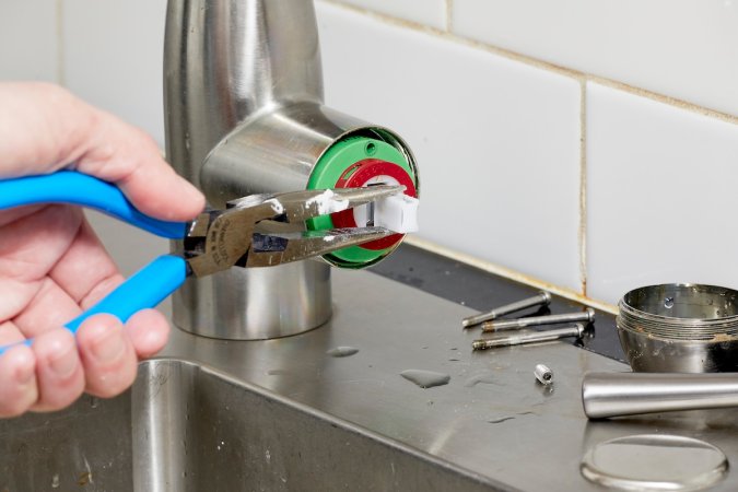 Person uses needle-nose pliers to remove faucet cartridge from kitchen faucet.