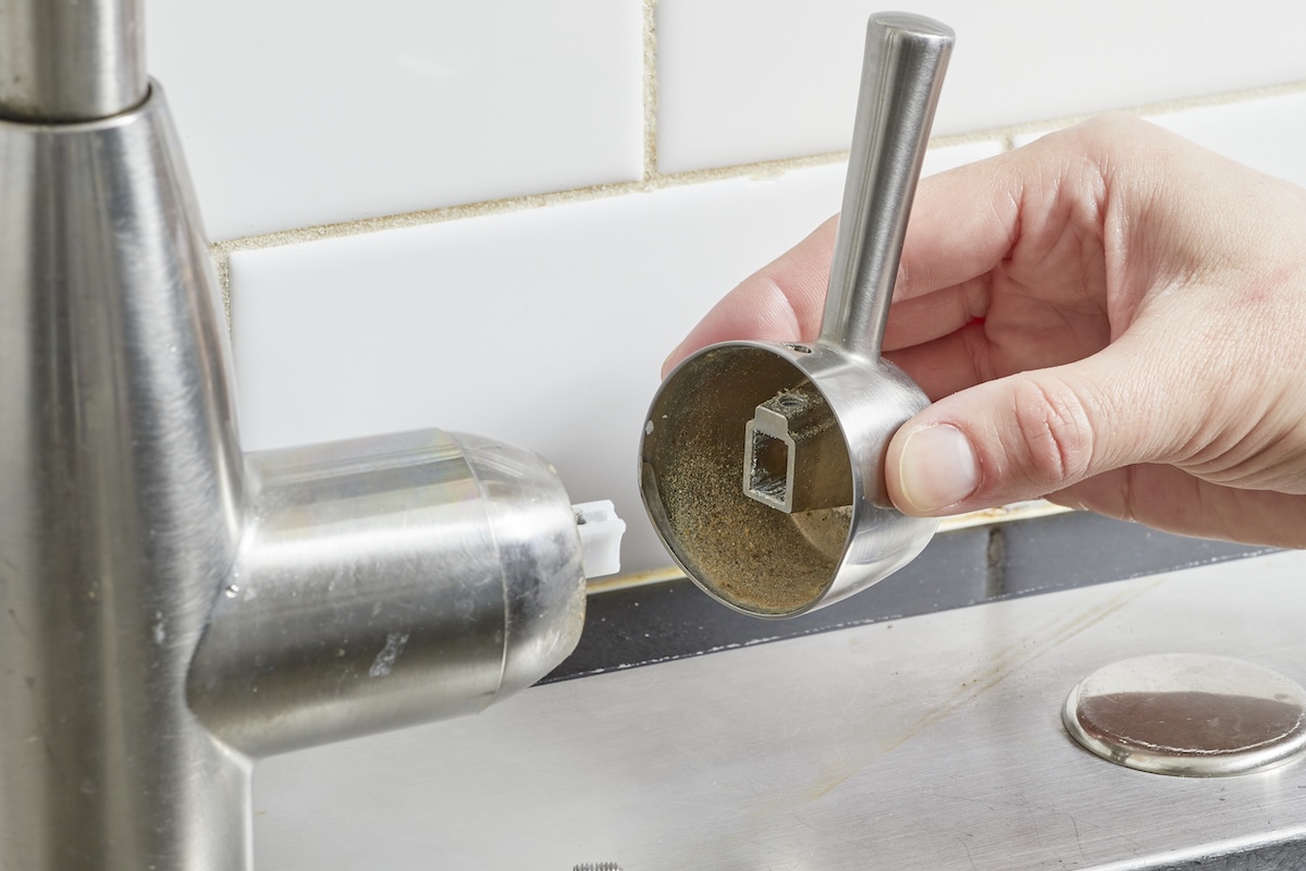 Woman removes the handle cap from a kitchen faucet.