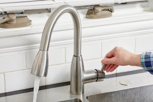 Woman pulls kitchen faucet on and water flows out.