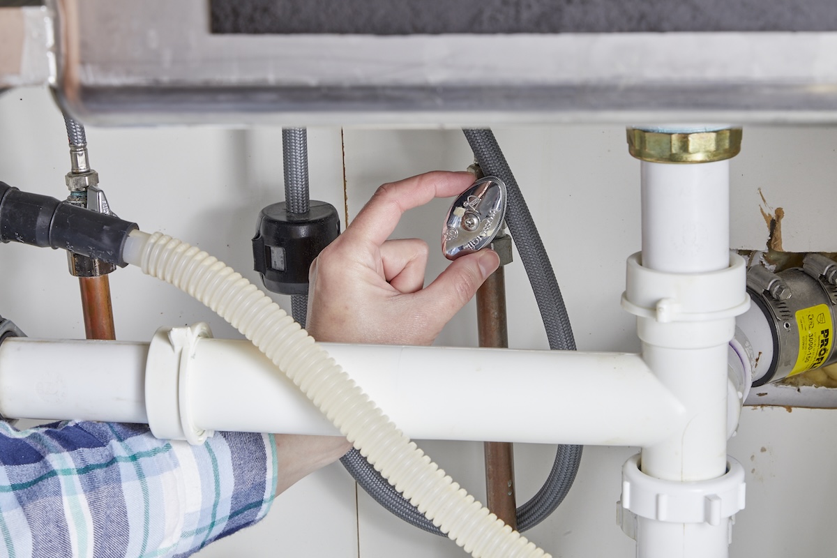 Person turns off water to faucet under the kitchen sink.