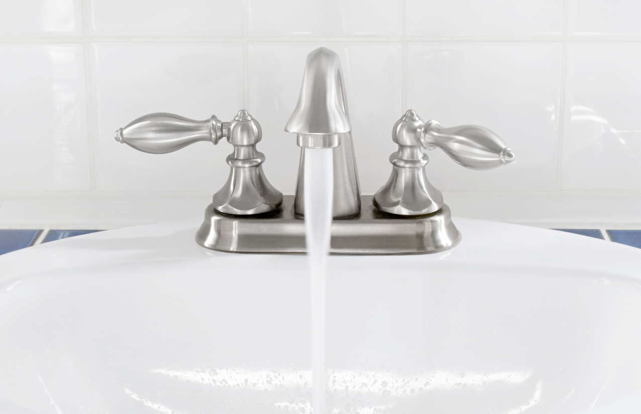 Brushed nickel faucet & handles with running water into white sink.