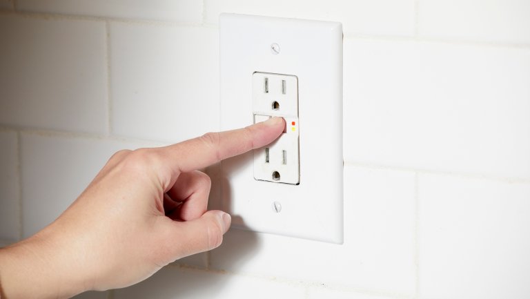 Woman resets the button on a GFCI outlet.