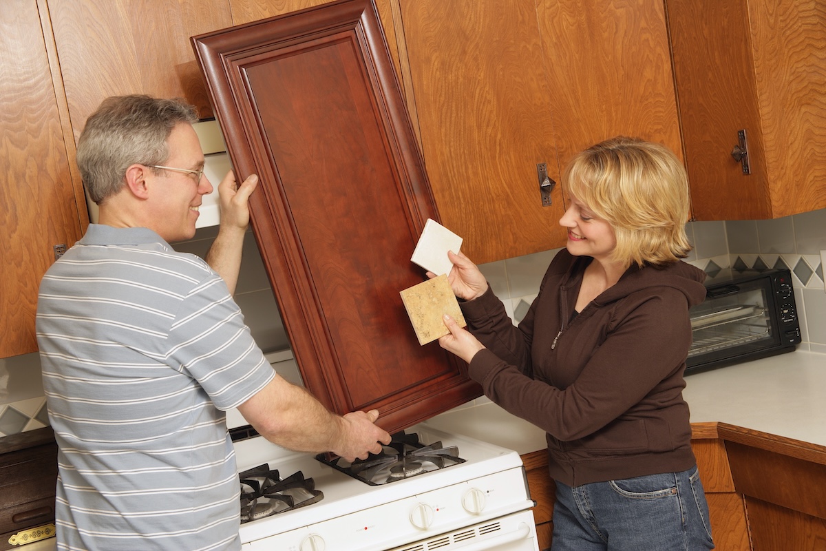 Couple holds color swatches to a cabinet front door in their kitchen.