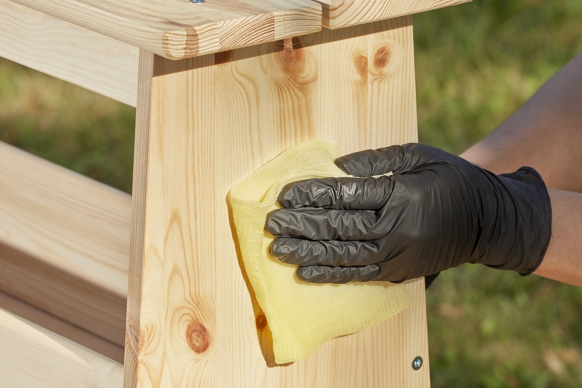 Cleaning wooden furniture with gloves on before staining it.