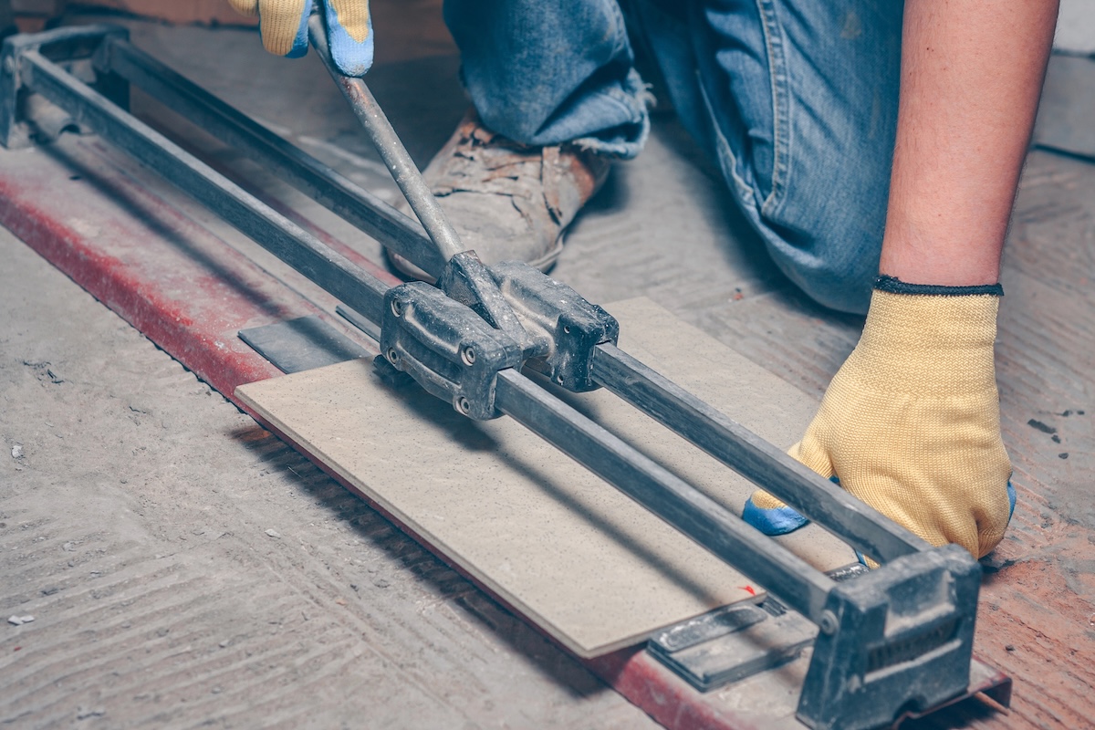 Man cuts tile using a manual tile cutter on the floor.