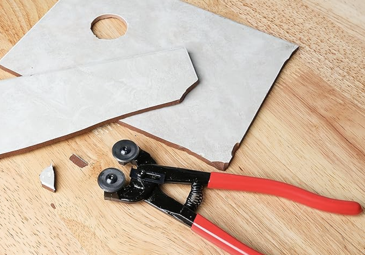 A pair of red nippers used to cut some grey tiling.