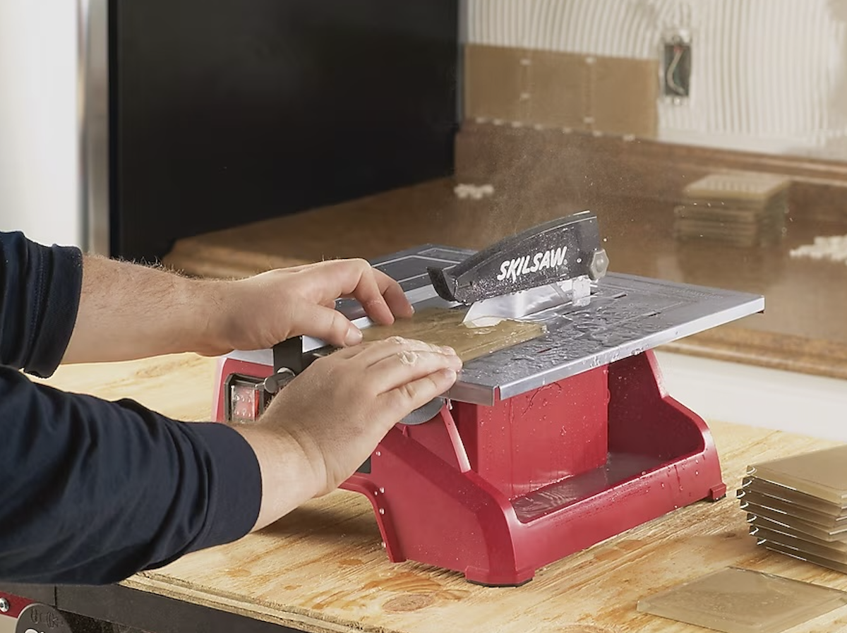 A man pushes a grey tile through the SKIL saw tile cutter.