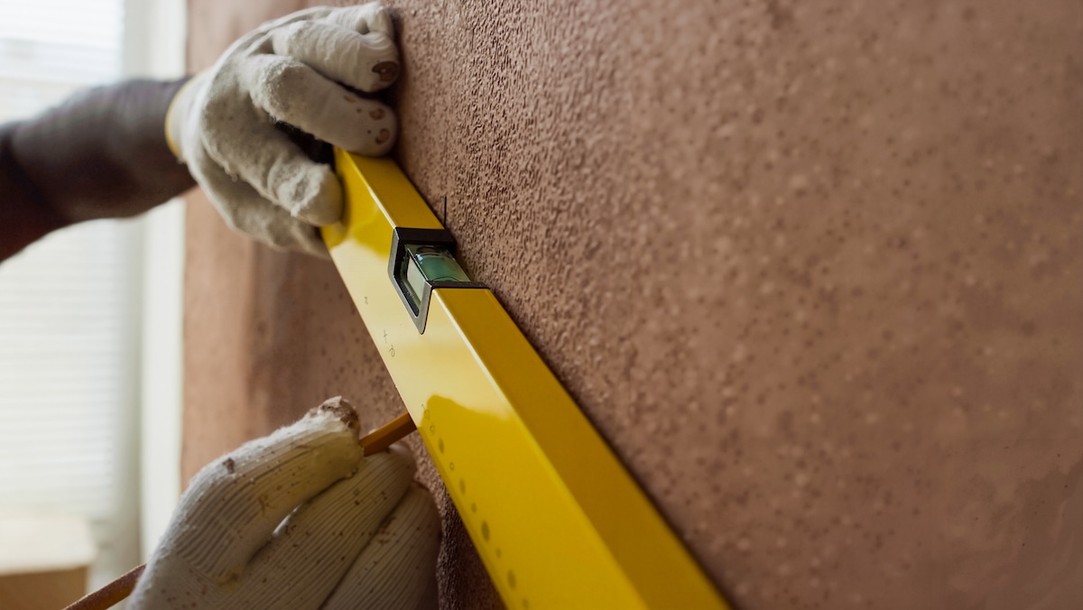 A pair of hands wearing safety gloves while using a yellow leveling tool.