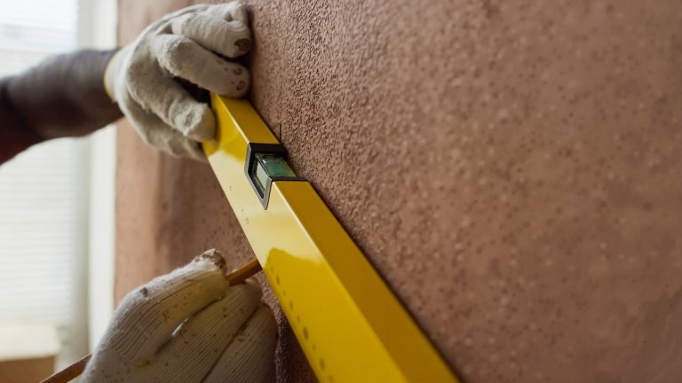 A pair of hands wearing safety gloves while using a yellow leveling tool.