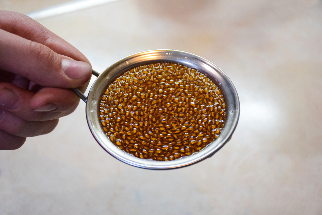 Human hand holds iron small sieve with small brown seeds