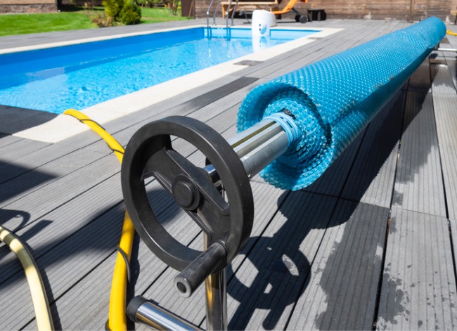 A pool cover on a spindle, with rectangular swimming pool in background.