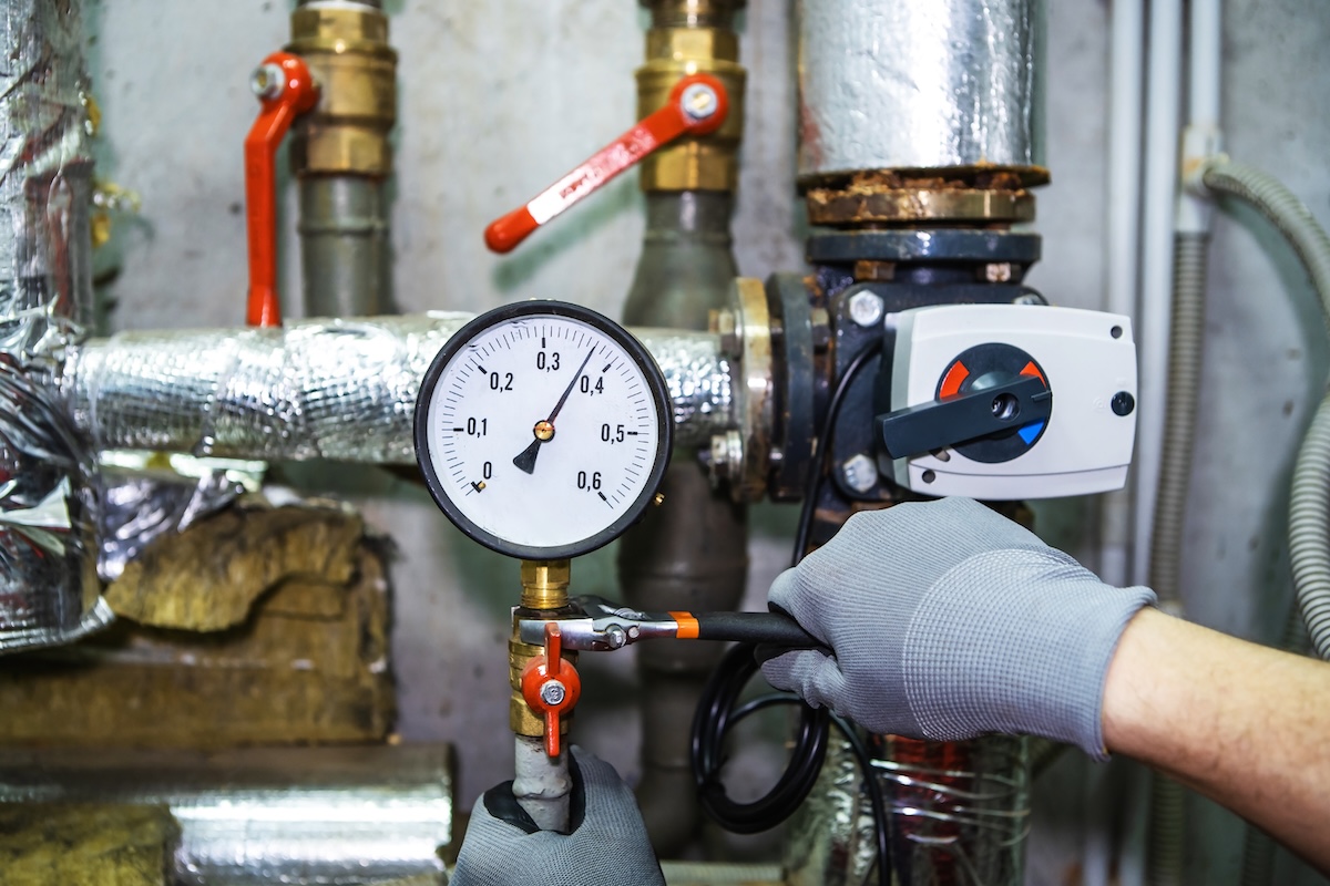 A plumber wear gloves as they attaches a screw on water pressure gauge to water pipes.