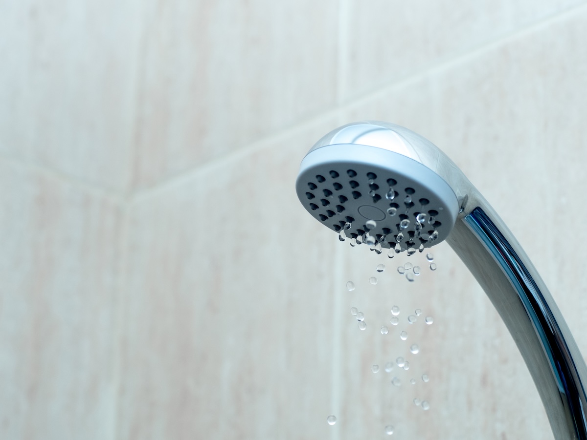 A shower head trickles a small stream of water because of low water pressure.