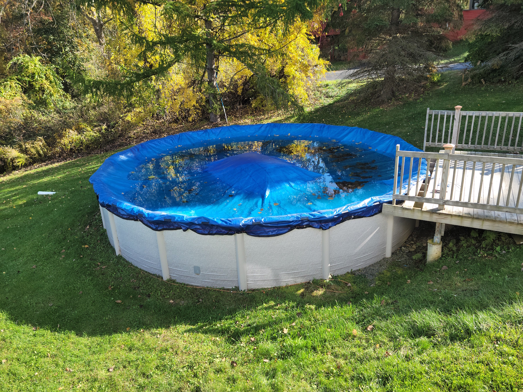 A large round pool closed for the winter with blue cover and wood deck.