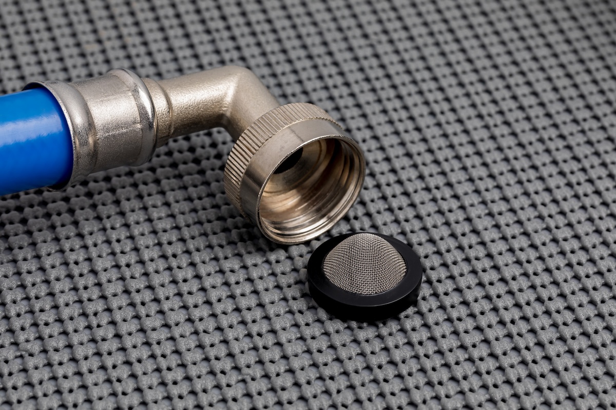 A small, mesh inlet screen sitting detached from the piping of a washing machine.