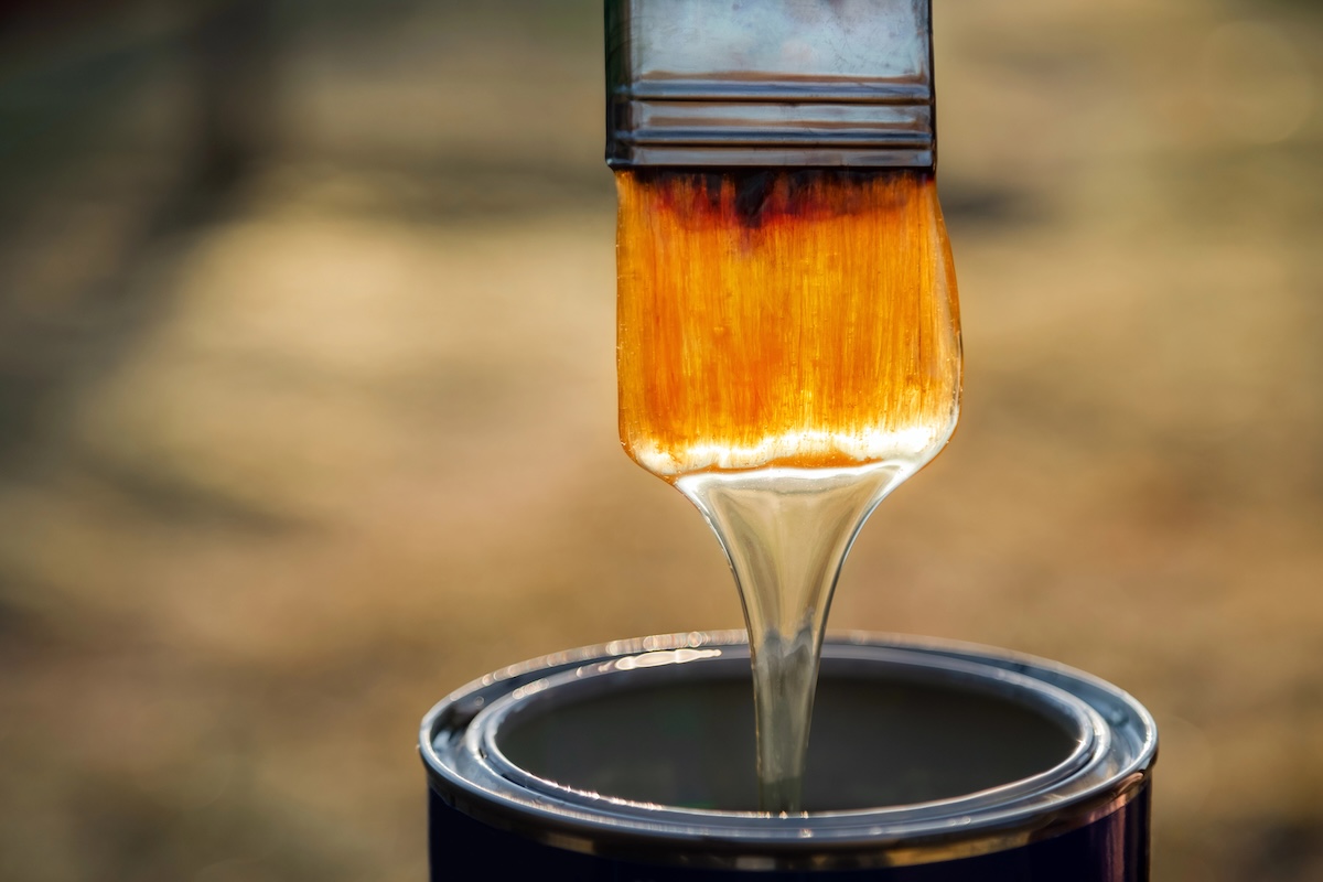 Close up of varnish dripping off paint brush and into the can.