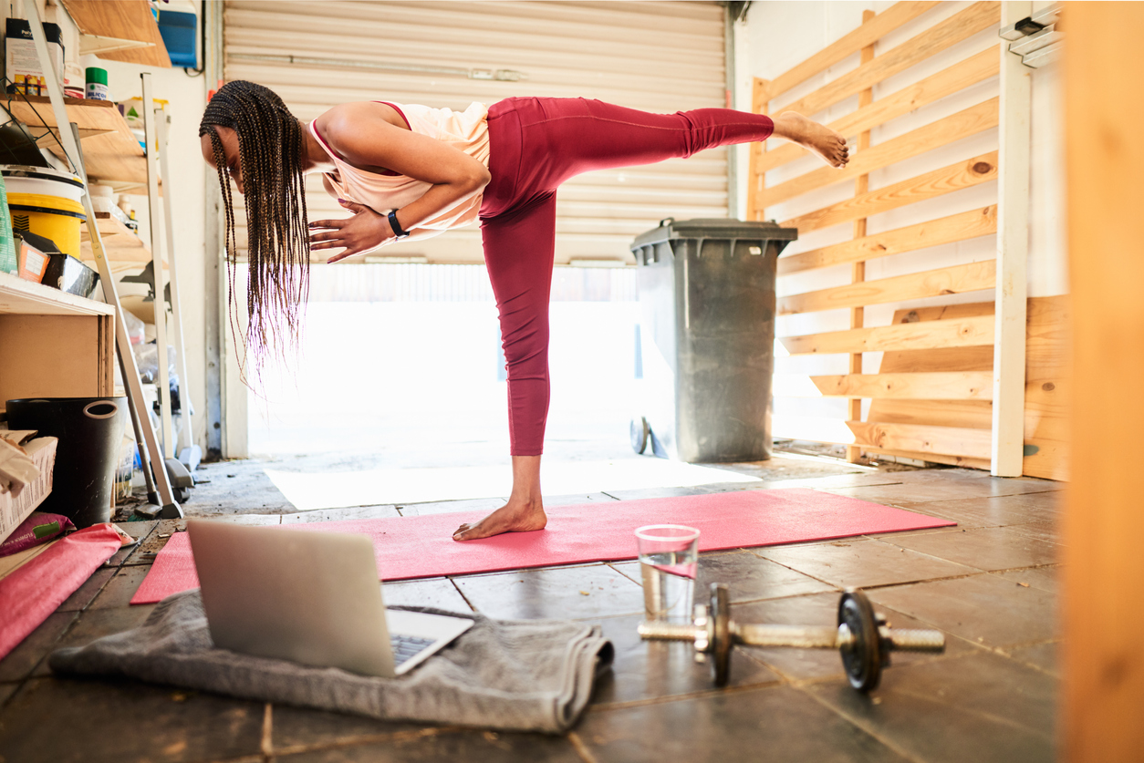 Young African American woman in sportswear practicing her warrior pose on an exercise mat in her garage during an online yoga class